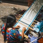 A woman weaves vibrant textiles outdoors in Antigua Guatemala.
