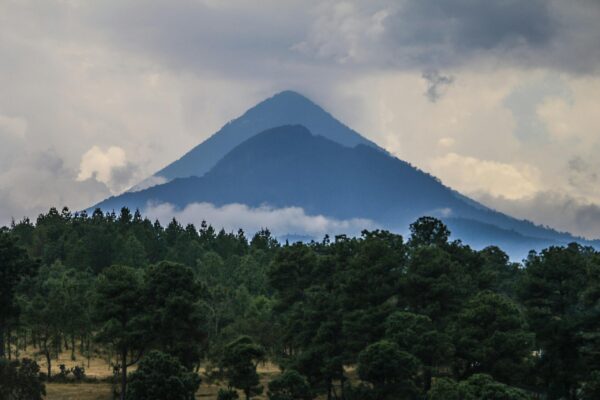 Majestic volcano rises above lush forest in Salcajá, Guatemala, shrouded in clouds.