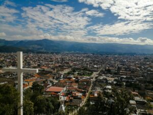 Panoramic view of Quetzaltenango, Guatemala with a prominent cross and clouds in the sky.