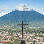 Scenic view of Antigua Guatemala with Volcán de Agua, featuring a prominent cross in the foreground.