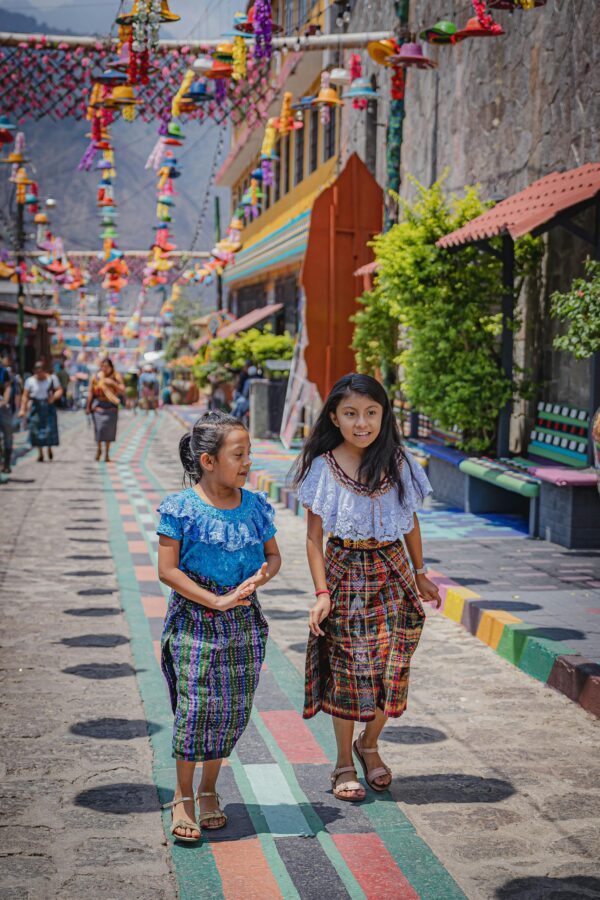 Two girls in traditional attire walking on a vibrant street in Panajachel, capturing cultural essence.