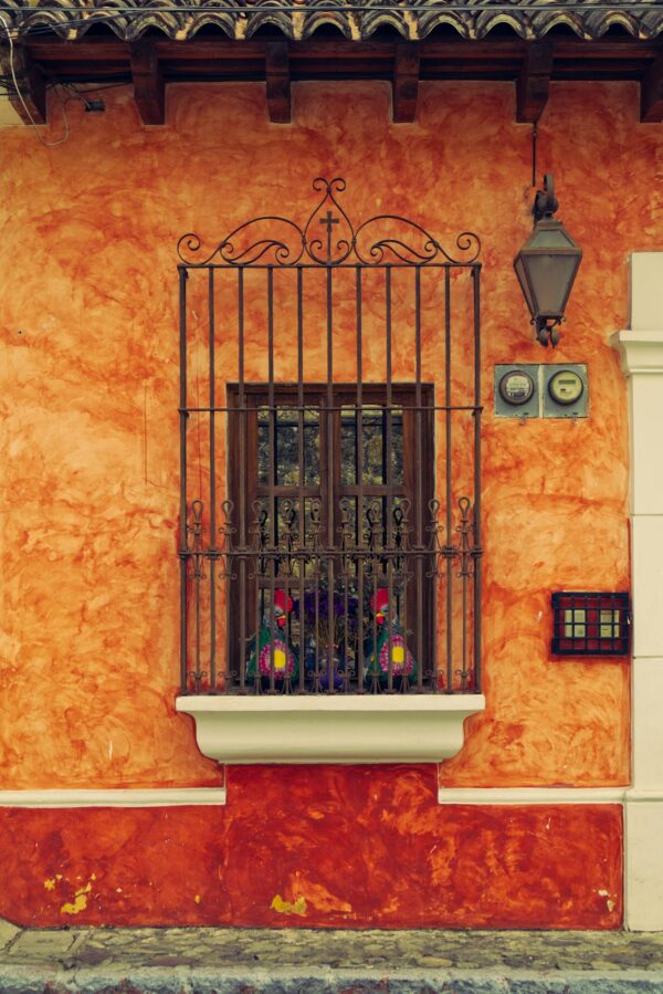 Vibrant colonial facade in Antigua with wrought iron window and orange walls.