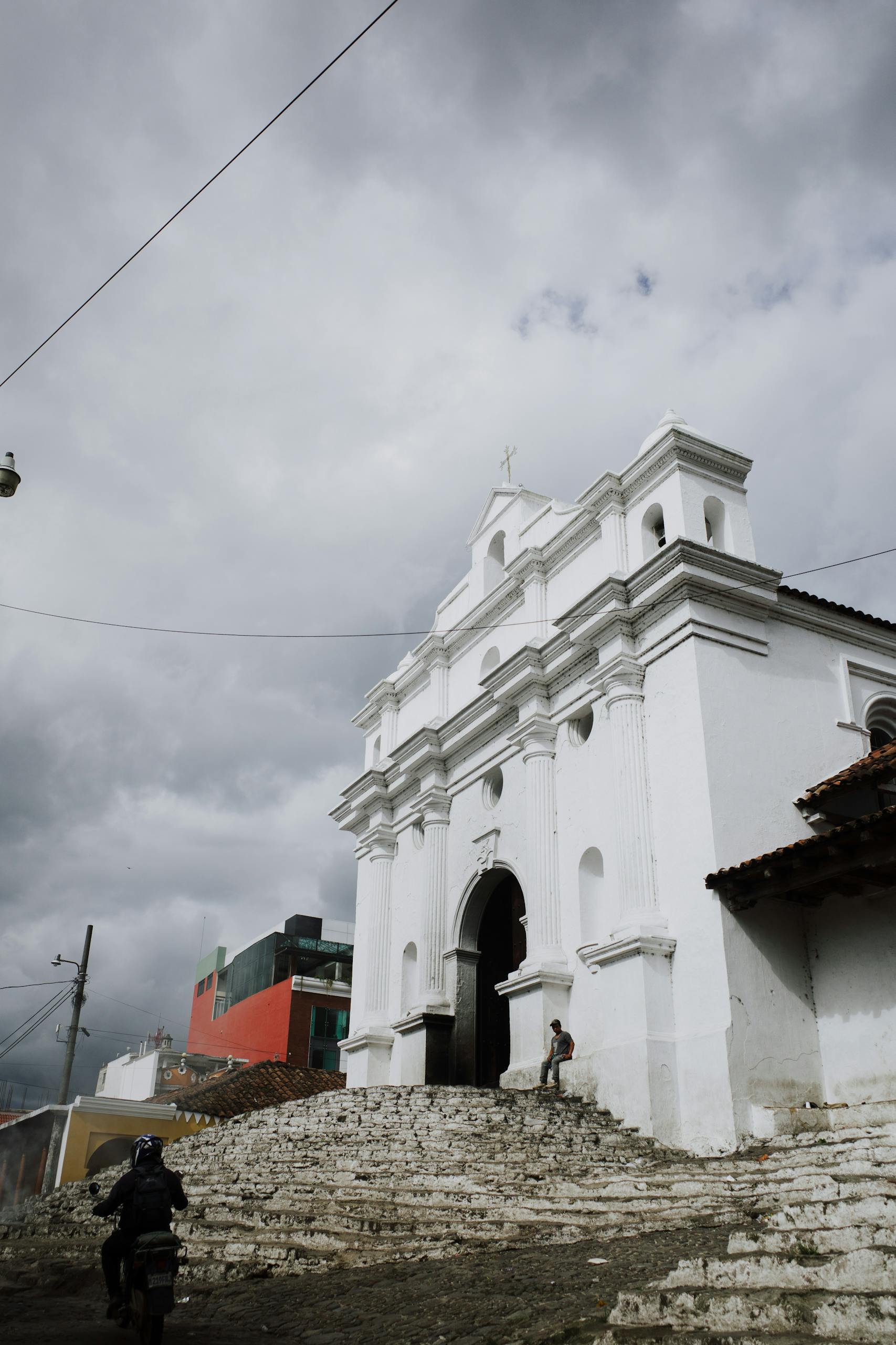 White colonial church with cloudy backdrop in Chichicastenango, Guatemala, showcasing local culture and architecture.